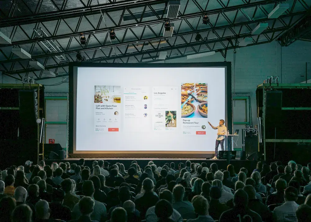 A finished website shown on a large screen to a seated audience.