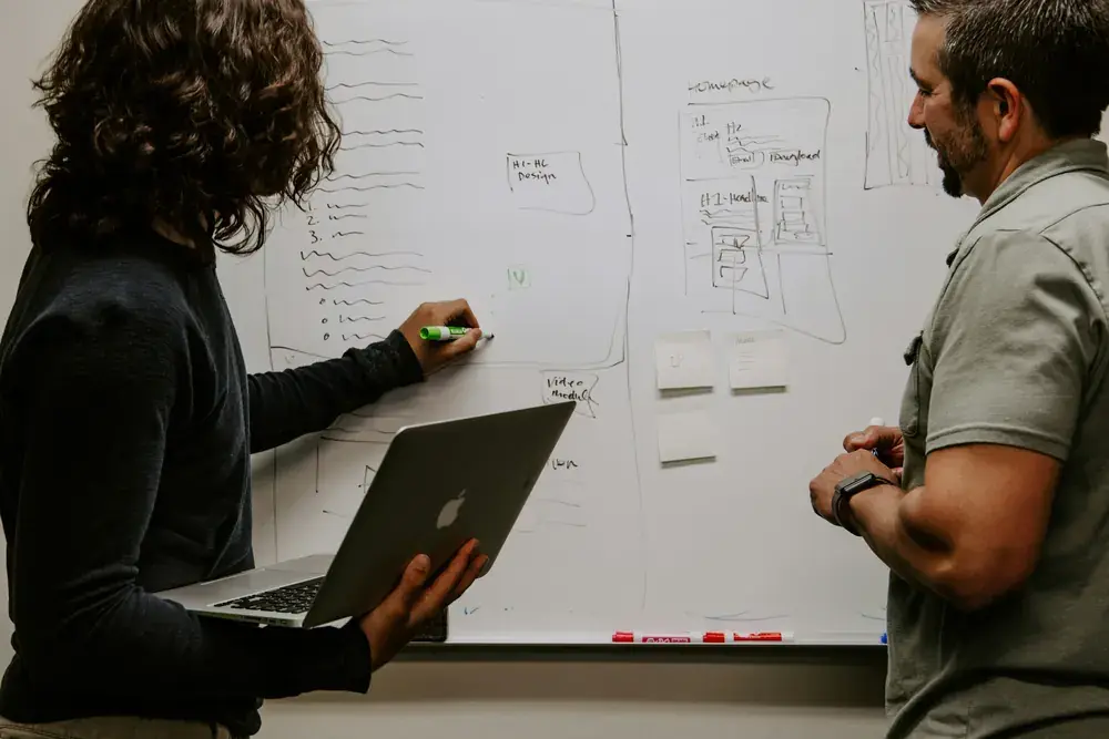 Two people mapping out a plan on a whiteboard.