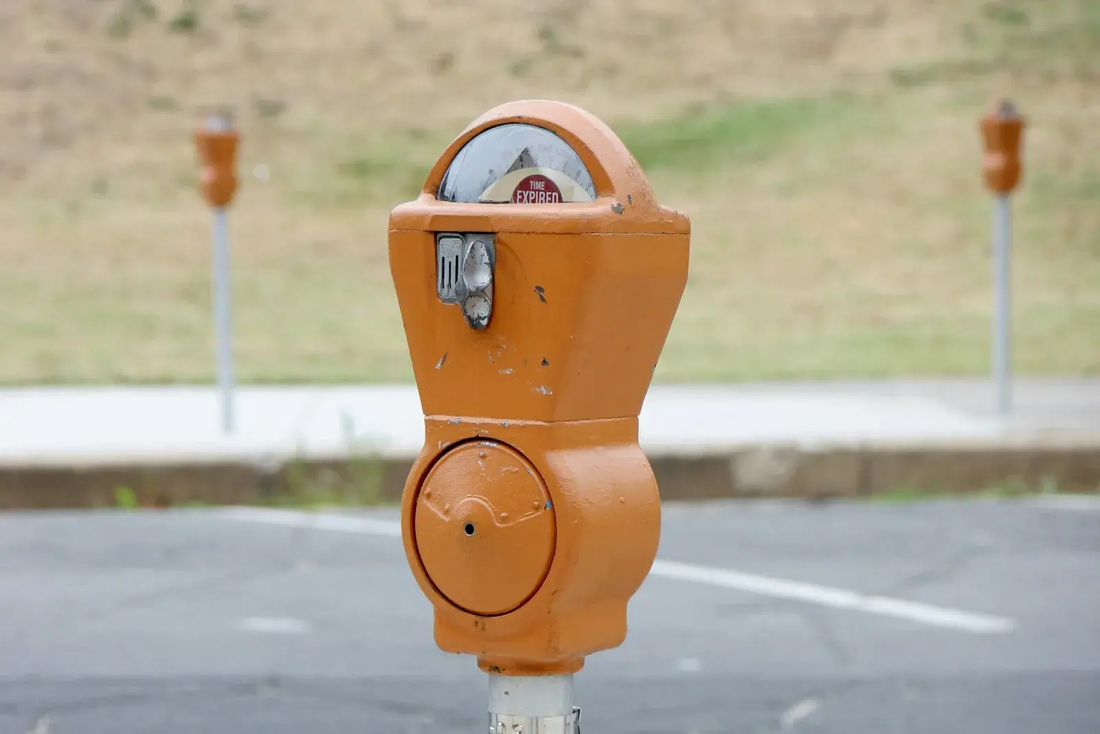 An orange parking meter on the edge of an empty lot, its dial reading TIME EXPIRED.