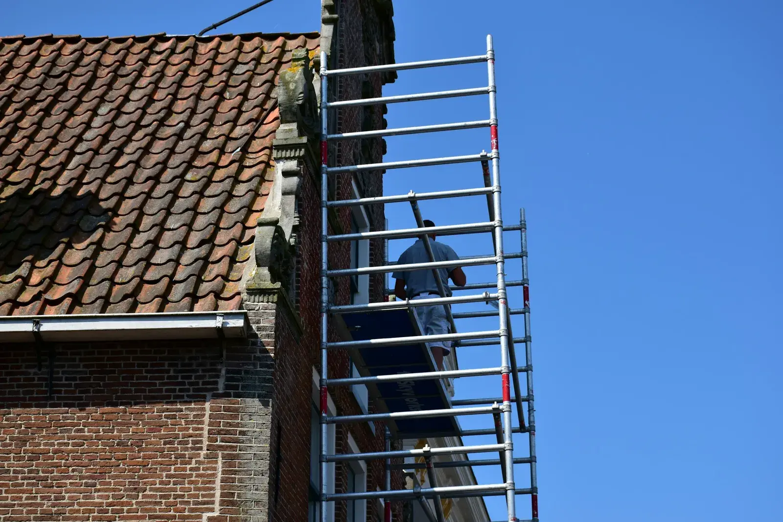 A worker on metal scaffolding against the brick gable end of an old building.