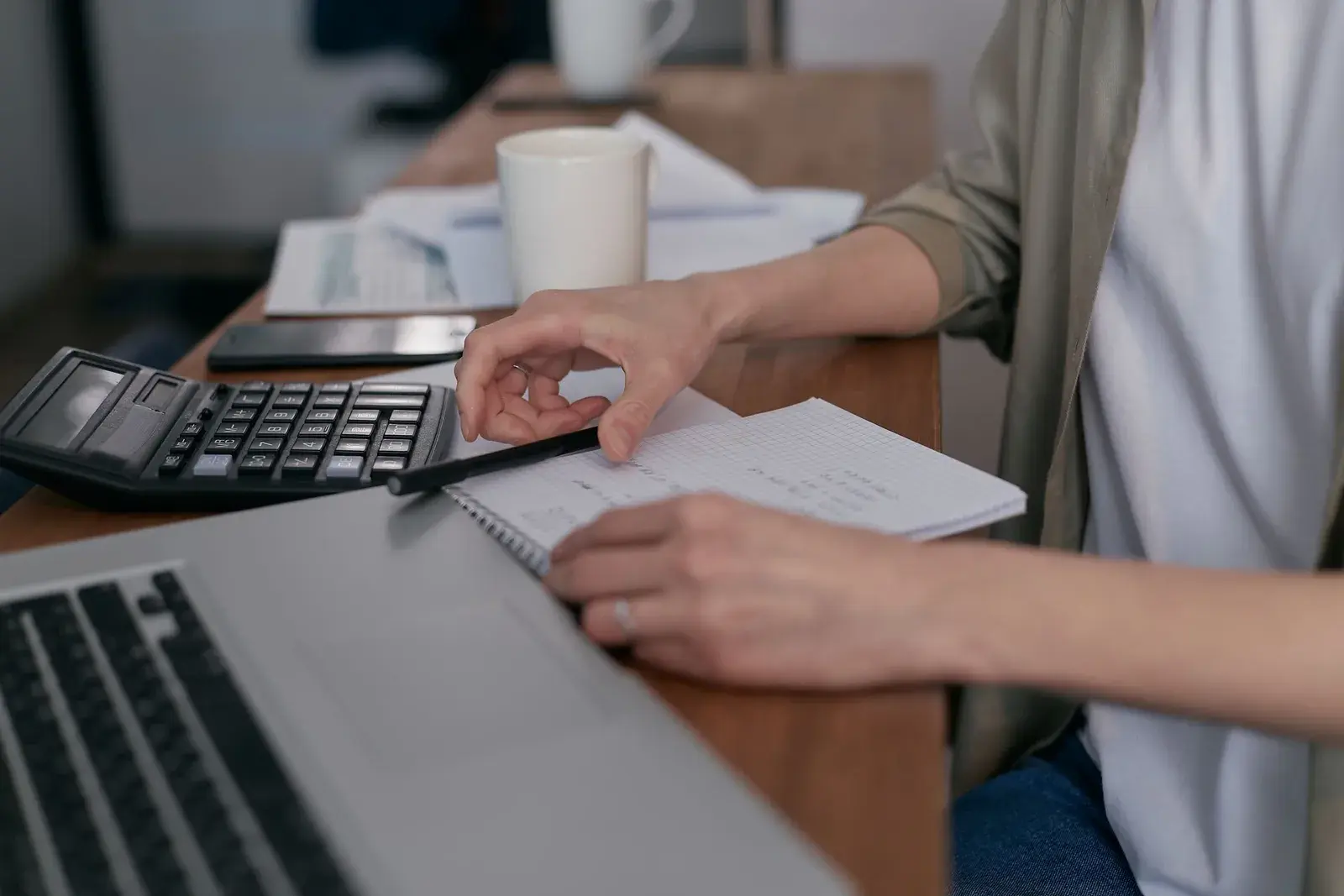 Someone working through figures on a notepad beside a calculator and laptop.