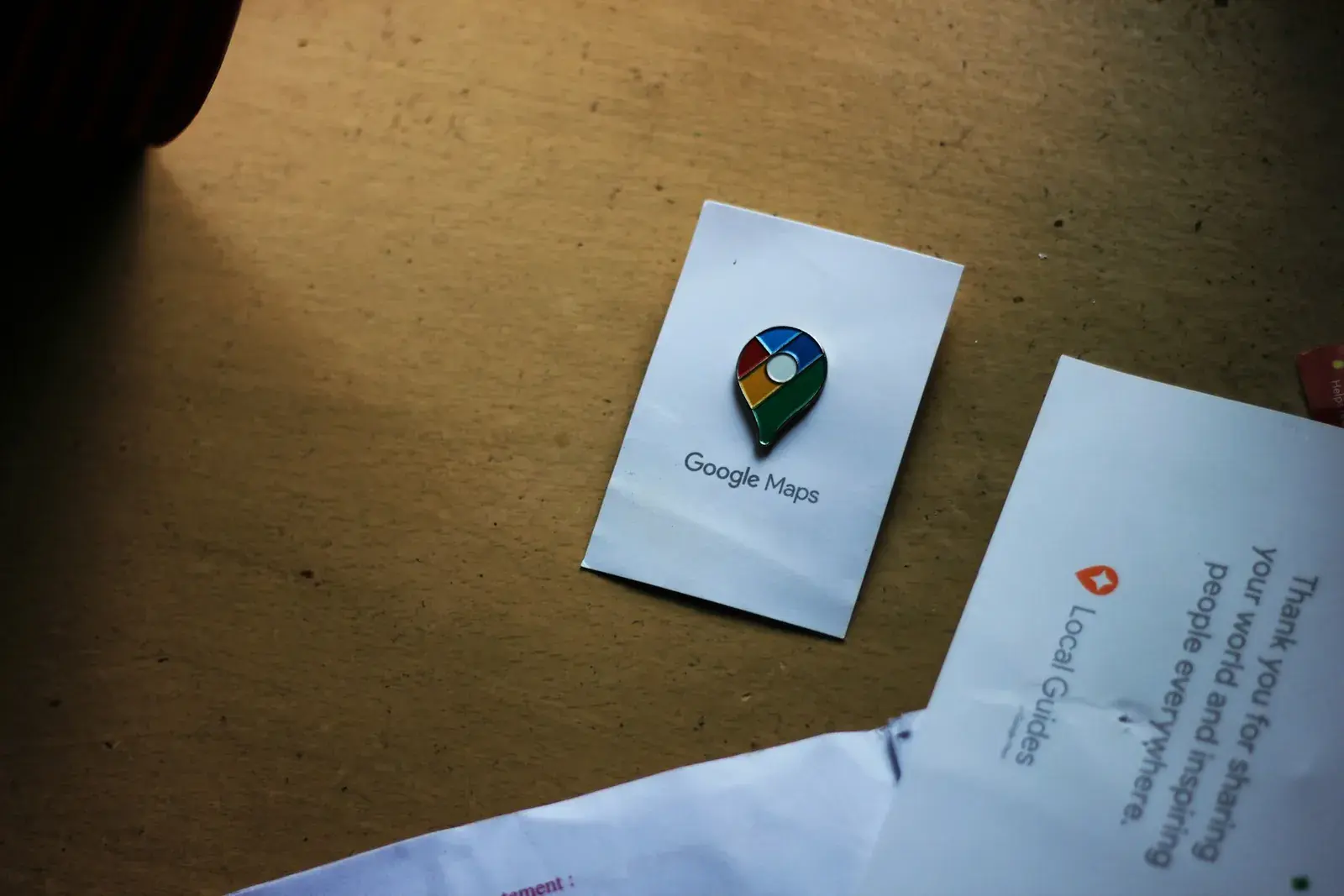 A Google Maps pin printed on a card lying on a wooden desk.