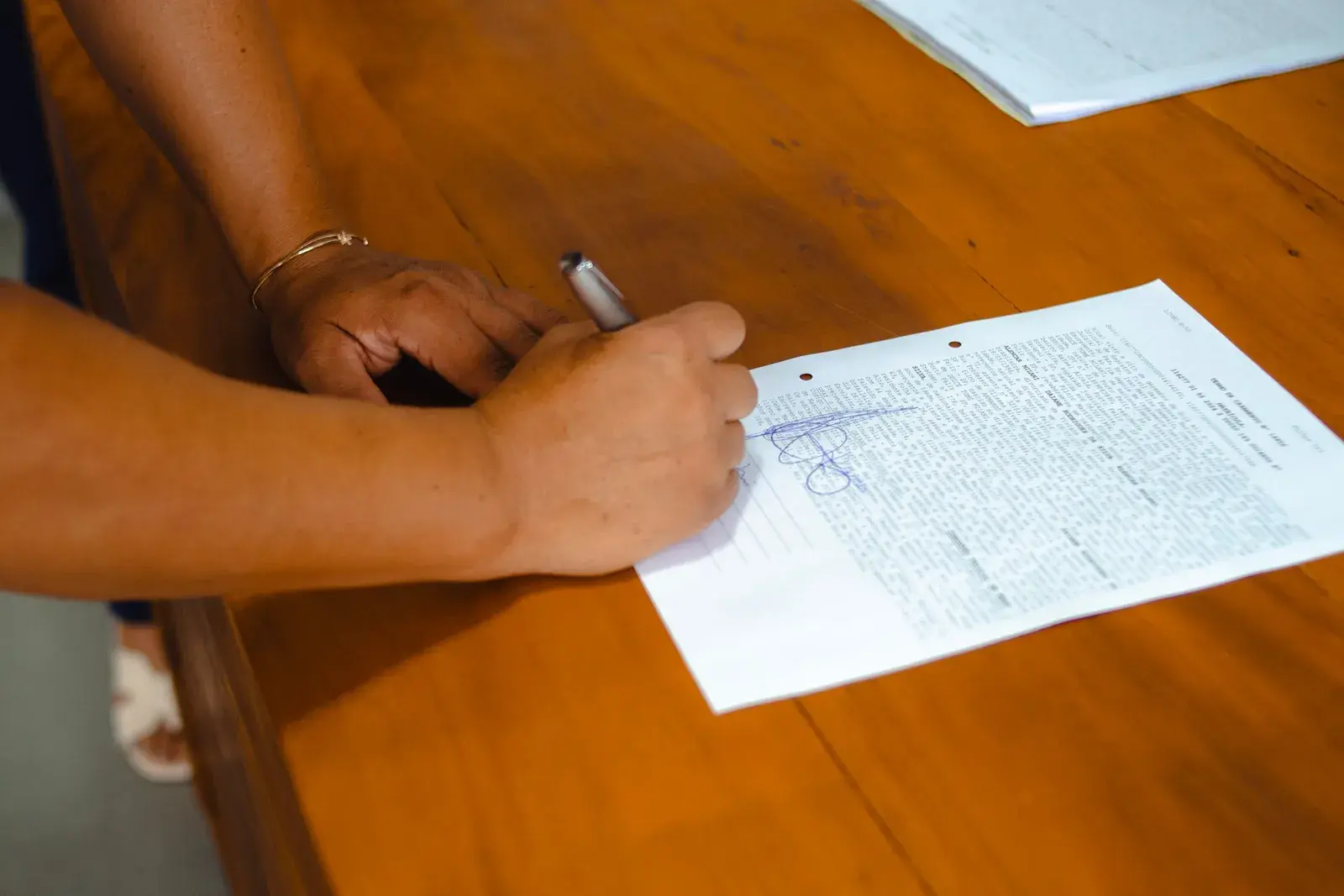 A hand signing a document at a wooden table.