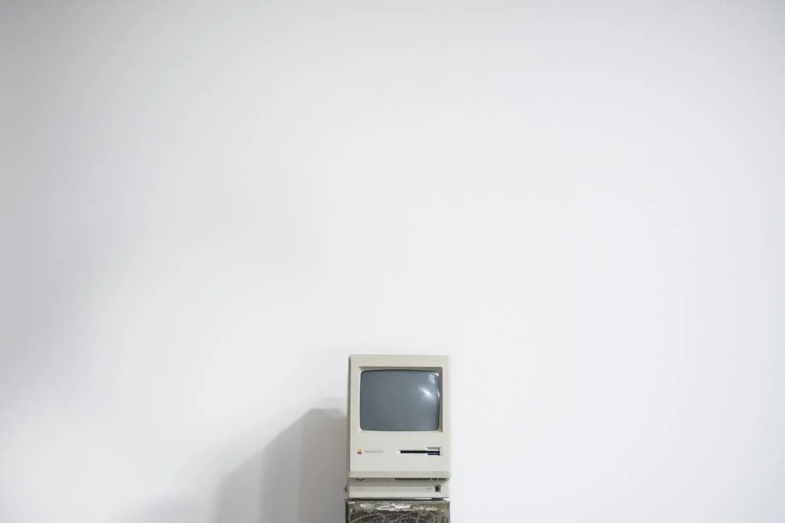 An old Macintosh Plus computer, switched off, sitting alone against a plain wall.