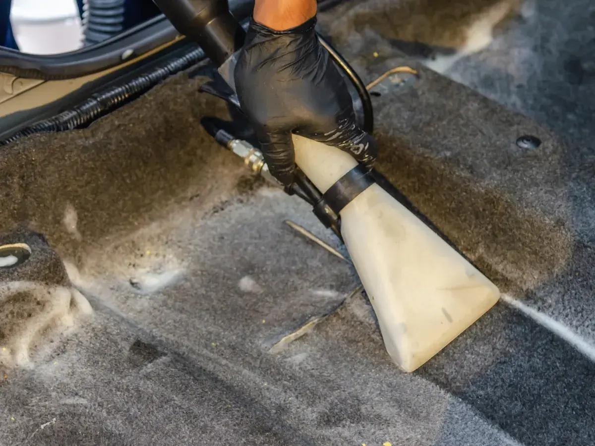 A gloved hand vacuuming dirt out of a car's carpet.