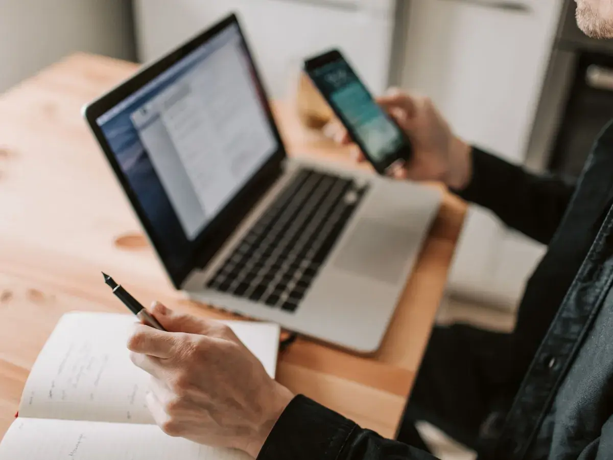 A laptop open on a list of enquiries with a phone in hand beside it.