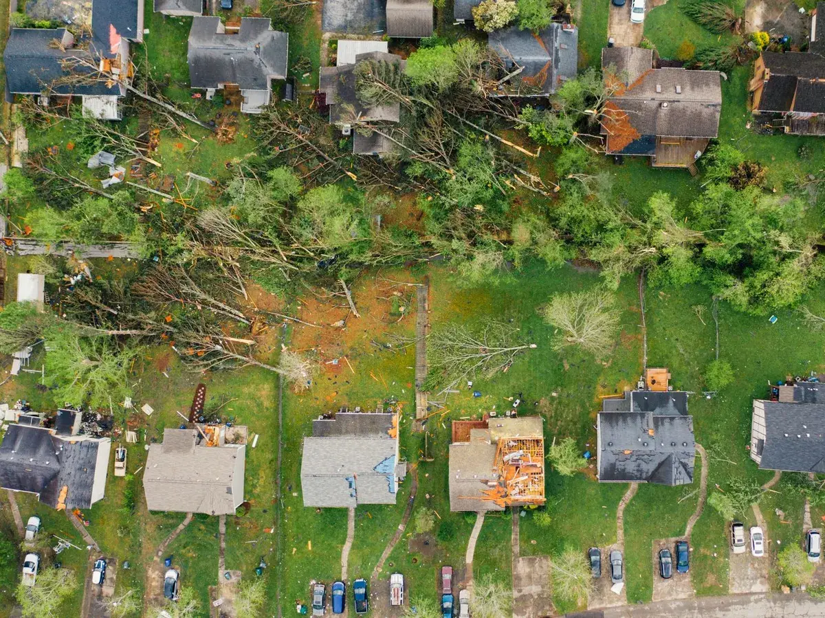 An aerial view of a suburban street after a storm, with trees down and roofs damaged.