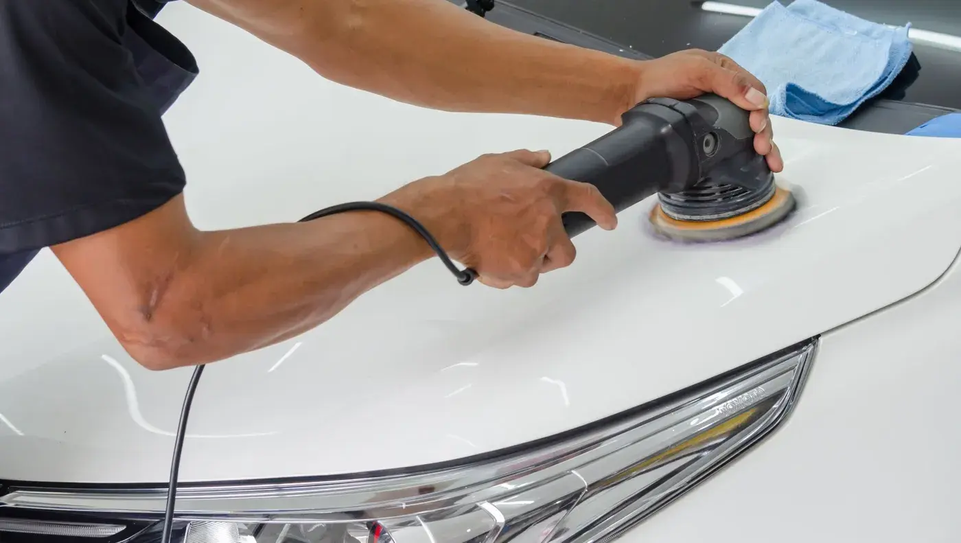 A detailer running a dual action polisher across the hood of a white car.