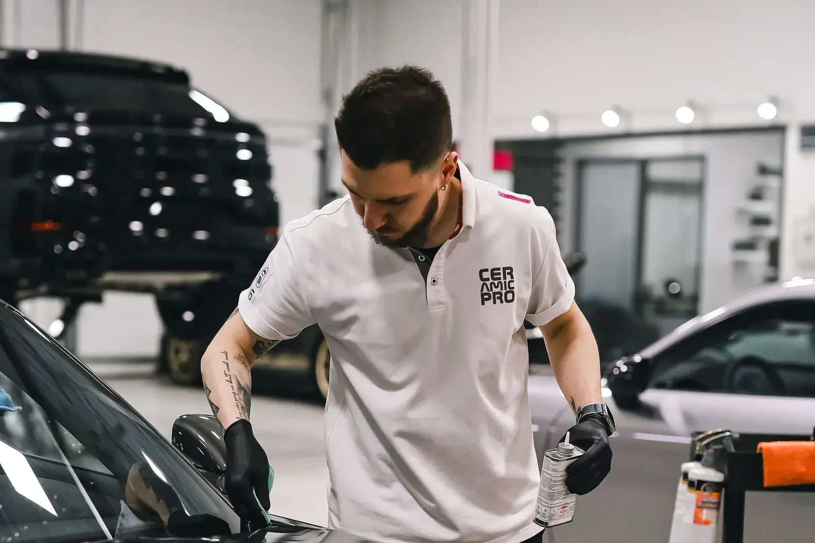 A detailer in a shop uniform working along the edge of a black car panel.