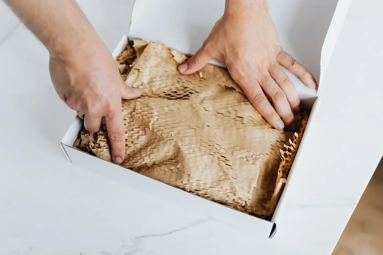 Hands folding protective paper over an item in a shipping box.