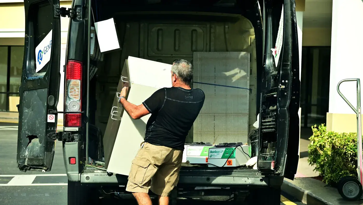 A worker lifting an old appliance into the back of a van.