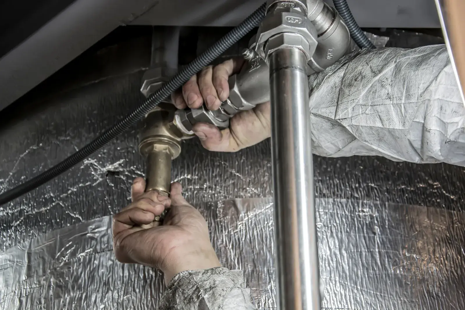 A plumber tightening a fitting on pipework under a fixture.