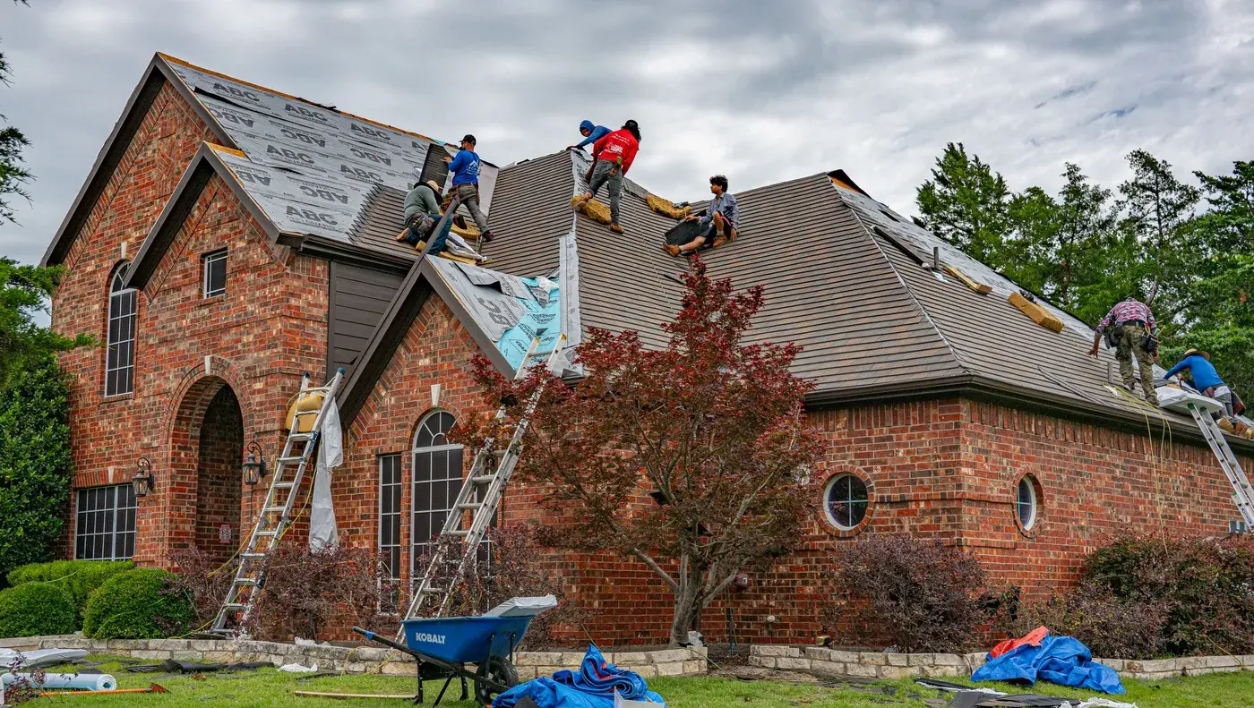 A crew re-roofing a two storey brick house with ladders against the eaves.