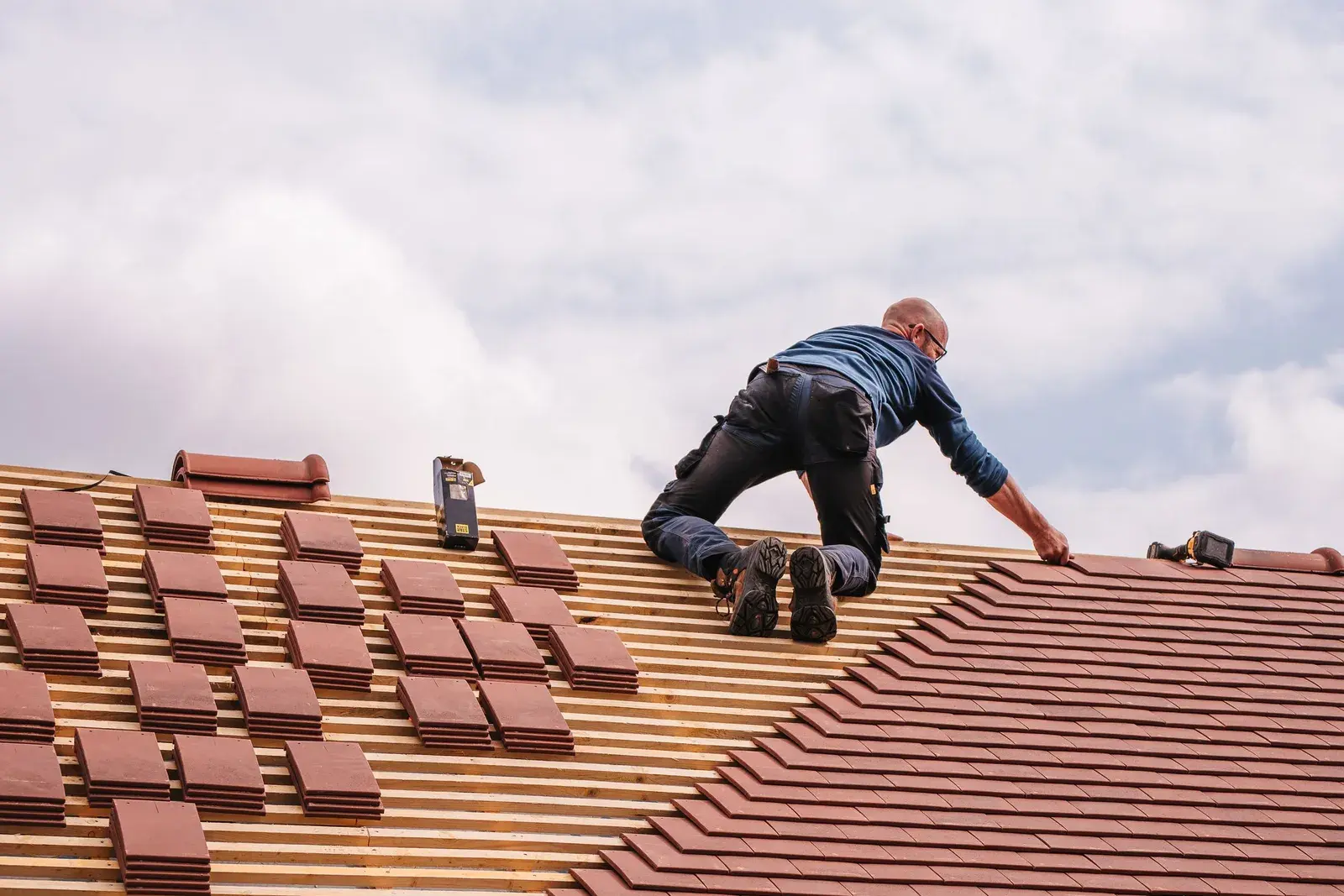 A roofer laying rows of clay tiles across a pitched roof.