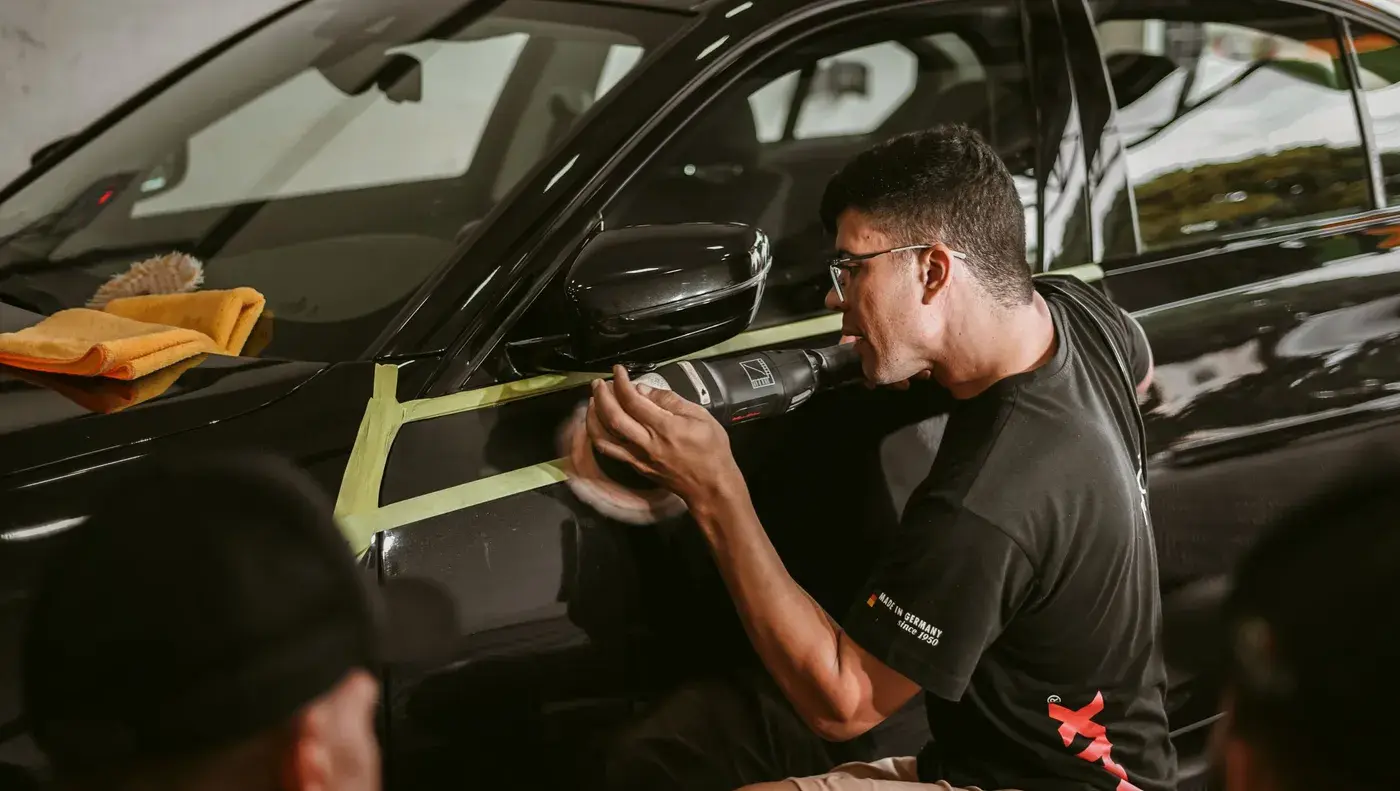 A detailer polishing a taped off panel on a black car.
