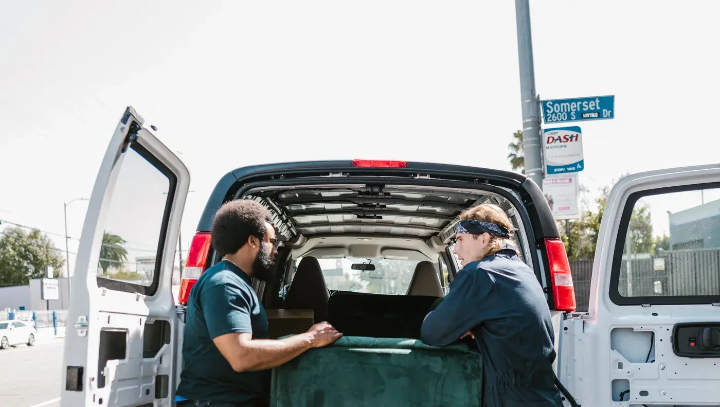 Two workers lifting a sofa into the back of a removal van.