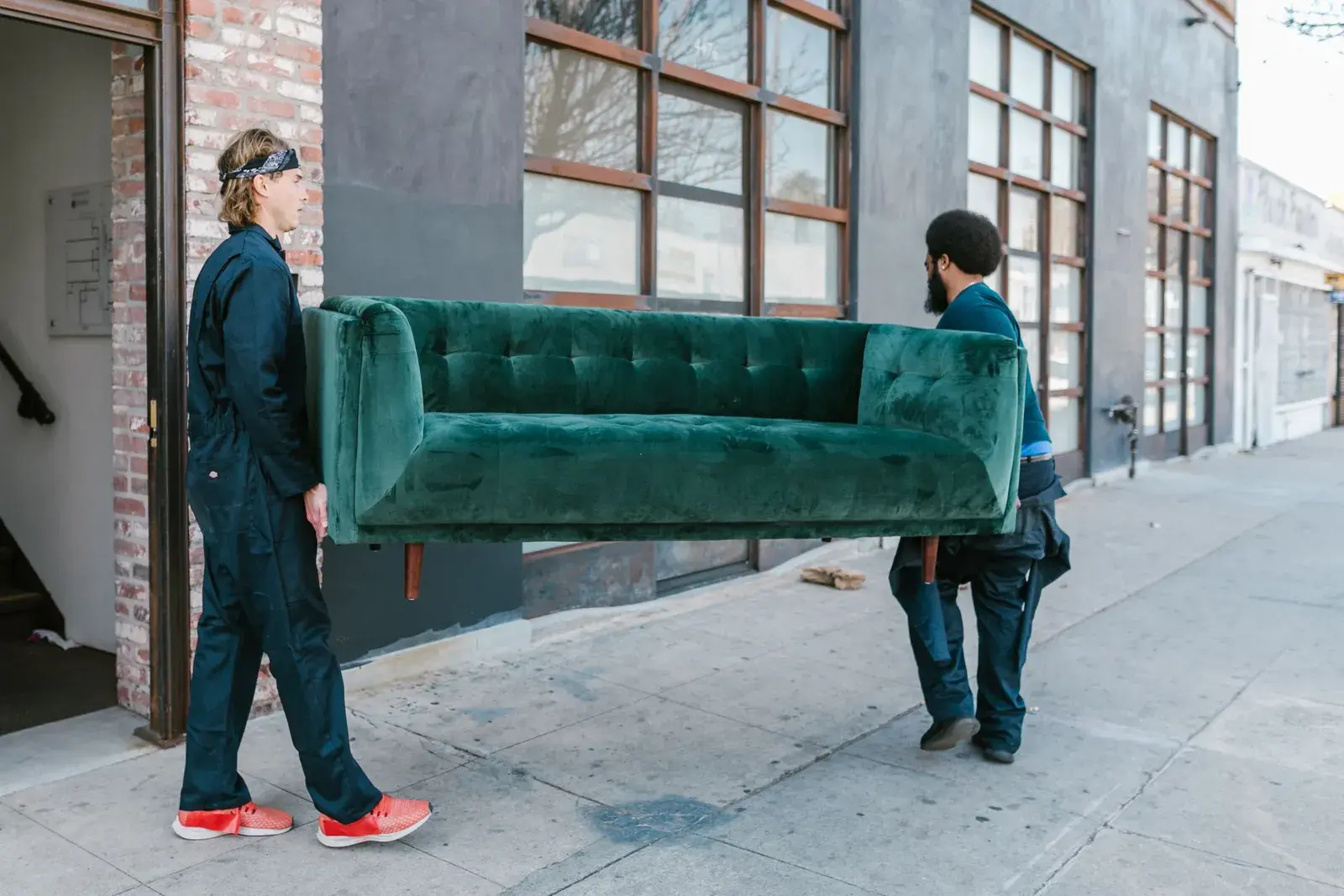 Two workers carrying a sofa out of a building during a cleanout.