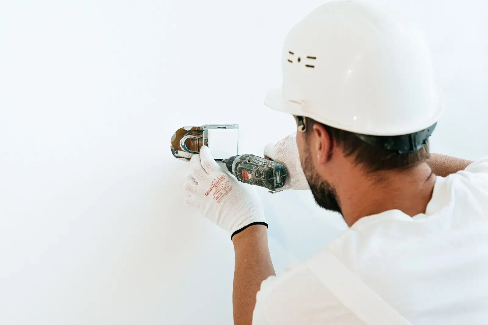 A tradesperson in a hard hat drilling into a wall on a job.