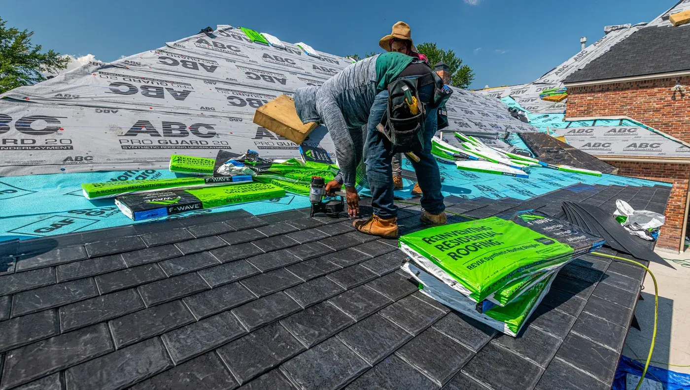A roofing crew spreading underlayment and stacking bundles across a residential roof.