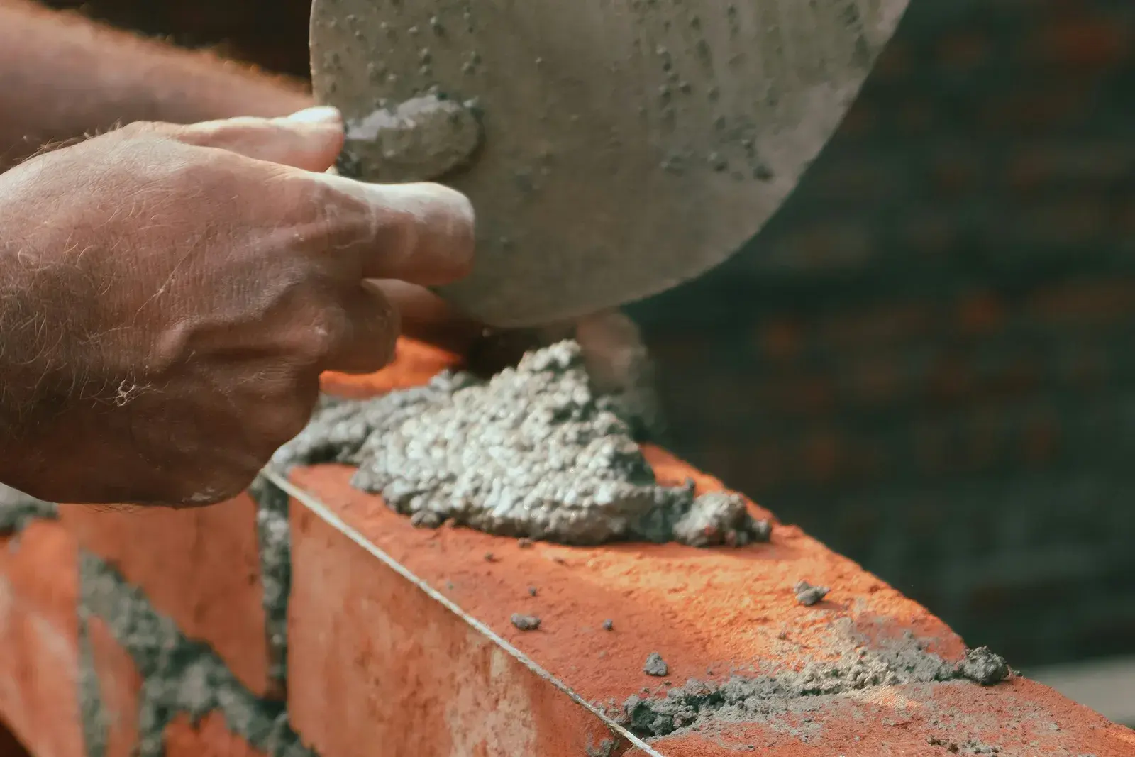 A bricklayer spreading mortar along a course of red brick with a trowel.