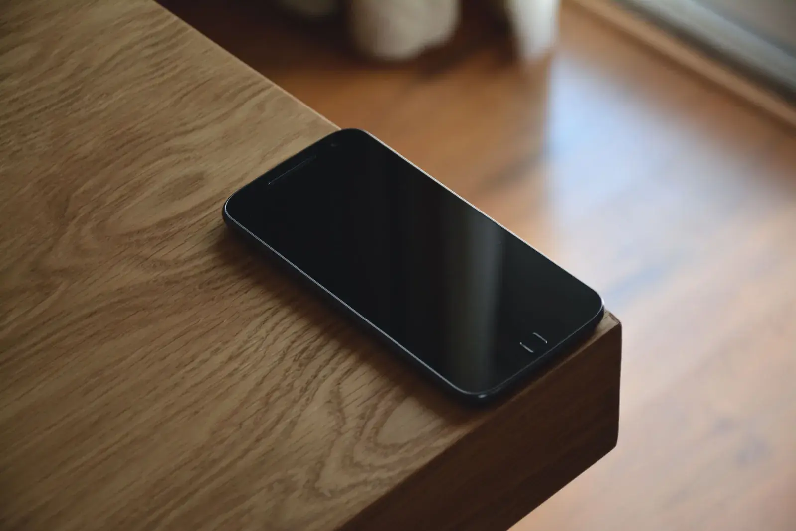 A phone sitting dark and silent on the edge of a wooden table.