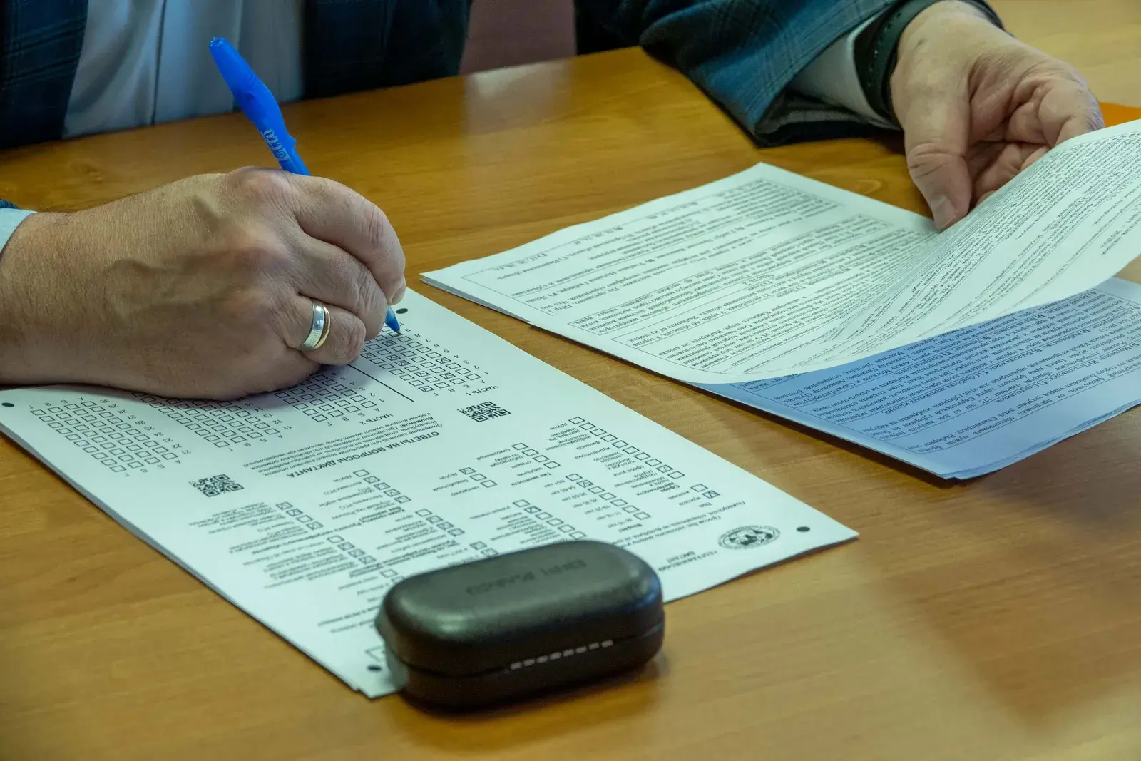Hands filling in an official form on a wooden table with a stamp beside it.