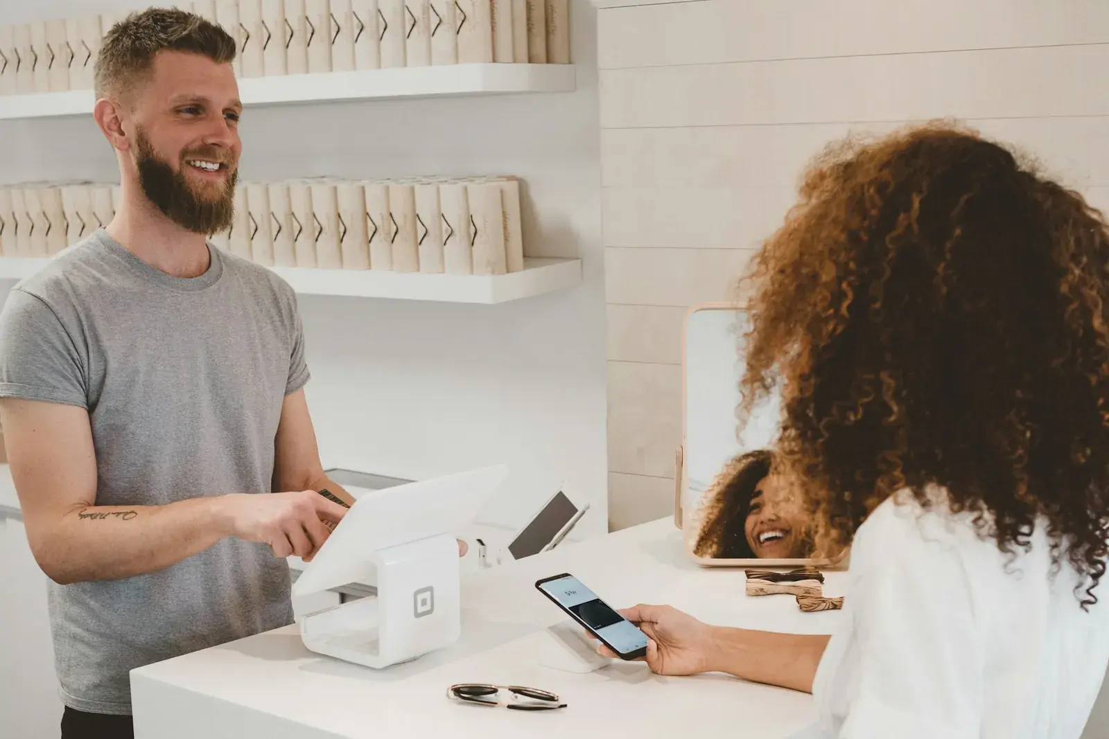 A shop owner serving a customer who is holding their phone at the counter.